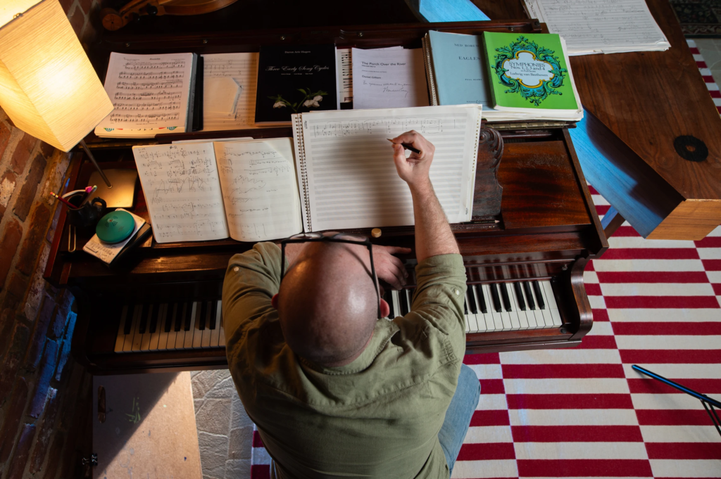 Bird's eye perspective of a person wearing a green shirt, sitting at a piano writing music